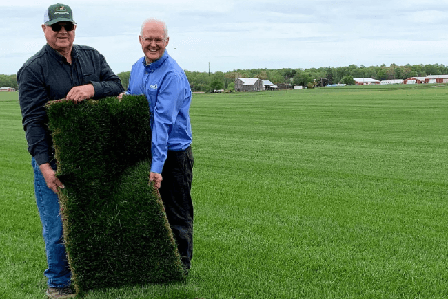 Two men holding a roll of turf on a farm.