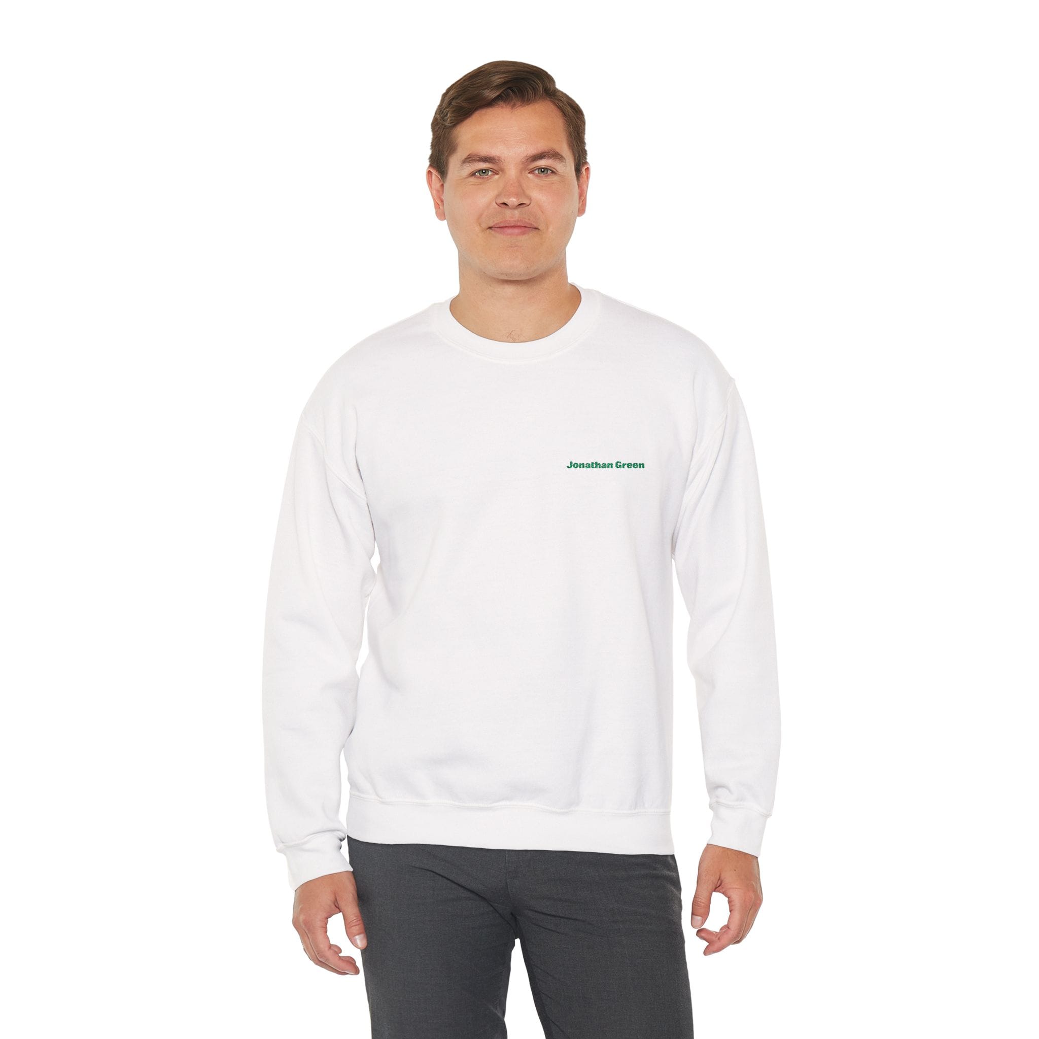 A man stands facing forward in the JG Embroidered Heavy Blend™ Crewneck Sweatshirt, a plain white design featuring "Jonathan Green" in small green lettering on the left chest, paired with dark pants.